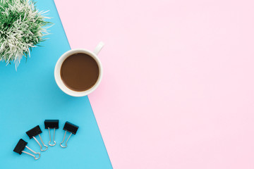 Creative flat lay photo of workspace desk. Top view office desk with clip, plant and coffee cup on blue pink color background. Top view with copy space, flat lay photography.