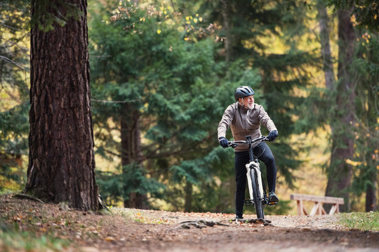 A senior man with electrobike cycling outdoors on a road in park in autumn.