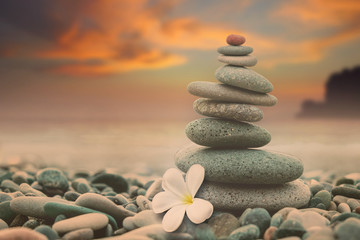 Pyramid of stones and a white flower on the beach by the sea on the background of a colorful sunset