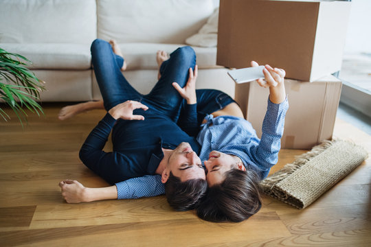A young couple with a smartphone moving in a new home, taking selfie.