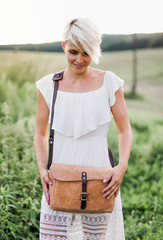 A front view of woman standing in nature with a brown leather bag. © Halfpoint