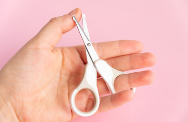 Female hand holding of little opened scissor for baby care. Close up of metal and plastic scissors for child care. Pink studio background. Concept of cutting baby nails.