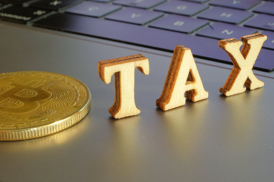 Bitcoin  and next to wooden with TAX letters. Bitcoin taxation concept