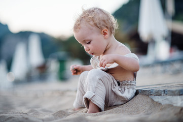A small toddler girl sitting on beach on summer holiday.