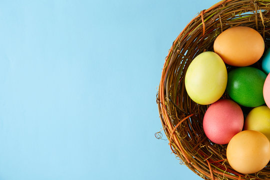 Beautiful easter table composition. Pile of painted eggs of different passtel colors in wicker basket on textured table background. Greeting card template. Copy space, close up.