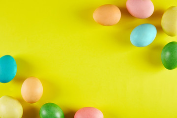 Bunch of blank painted Easter eggs of different pastel color on bright yellow paper background with a lot of copy space for text. Top view, flat lay, close up.