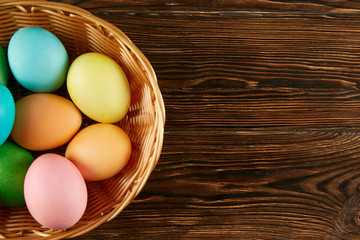 Beautiful easter table composition. Pile of painted eggs of different passtel colors in wicker basket on textured table background. Greeting card template. Copy space, close up.