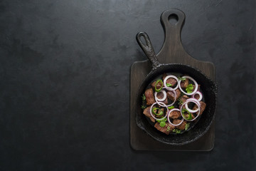 Pieces of roast beef in an old black pan.