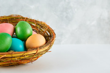 Beautiful easter table composition. Pile of painted eggs of different passtel colors in wicker basket on textured table background. Greeting card template. Copy space, close up.