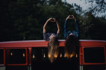 Two girl friends at dusk outdoors on a roadtrip through countryside, having fun.