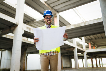 Portrait of male site contractor engineer with hard hat holding blue print paper