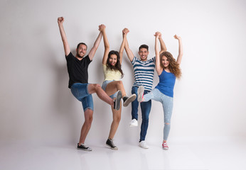 Obraz premium Portrait of joyful young group of friends standing in a studio, lifting legs.