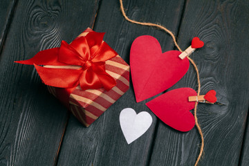 Gift box with red bow ribbon and  paper hearts on wooden background for Valentines day