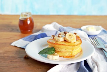 Cornmeal pancakes on a white plate. Served with bananas, walnuts and honey or maple syrup.