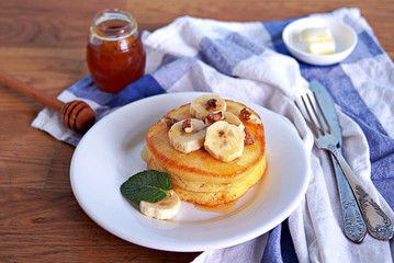 Cornmeal pancakes on a white plate. Served with bananas, walnuts and honey or maple syrup.