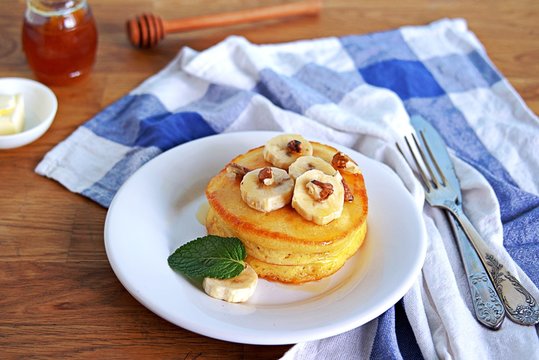 Cornmeal pancakes on a white plate. Served with bananas, walnuts and honey or maple syrup.