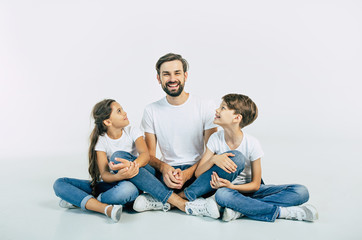 Handsome young father, attractive son and cute daughter are sitting together on the floor and hugging each other with happy and smiling faces. Best family