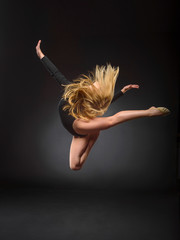 Young beautiful white caucasian girl gymnast with long hair jumps on black background.