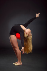 Obraz premium Young beautiful white caucasian girl gymnast with long hair doing gymnastic exercise on black background.