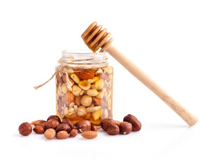A honey jar with a spoon for honey and different nuts on white background