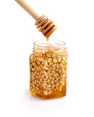 A honey jar with pine nuts and a spoon for honey on white background