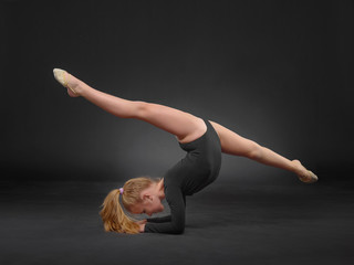 Obraz premium beautiful white caucasian girl gymnast doing gymnastic exercise for flexibility and stretching on black background.