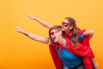 Beautiful mother and her cute little girl playing together dressed like superheros over yellow...