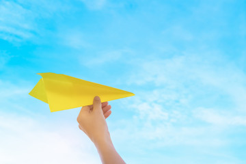Woman hand holding paper airplane on blue sky and white clouds abstract background.