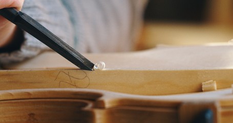 Macro close up of professional master artisan luthier painstaking detailed work on wood violin in a...