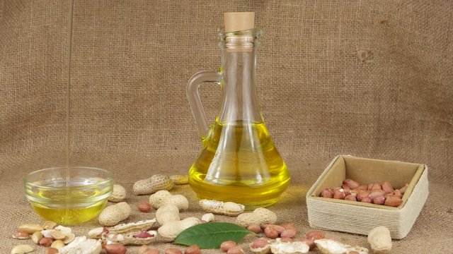 Groundnut oil is poured into a glass bowl. Glass bottle with groundnut oil on the background of peanut and parts of the peanut