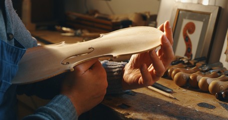 Close up of professional master artisan luthier painstaking detailed work on wood violin in a workshop. - obrazy, fototapety, plakaty