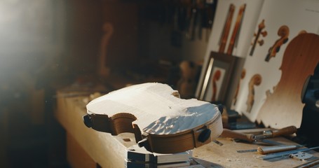 Close up of raw violin with different violin maker work tools on workbench in a workshop of...