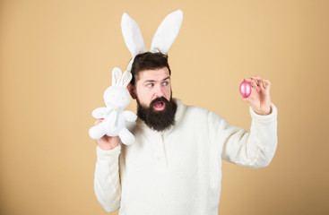 Easter is coming. Hipster with long rabbit ears holding egg laying hare. Bearded man with bunny toy and Easter egg. Celebration of spring time holiday. Easter bunny delivering colored eggs