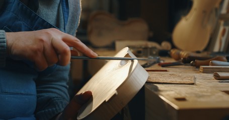 Close up of professional master artisan luthier painstaking detailed work on wood violin in a workshop. - obrazy, fototapety, plakaty