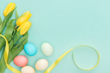 Top view of yellow tulips with ribbon and easter eggs isolated on blue