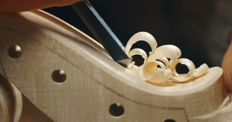 Macro close up of professional master artisan luthier painstaking detailed work on wood violin in a workshop.