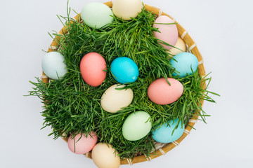 top view of colorful easter eggs in wicker plate with grass isolated on white