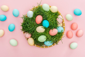 top view of easter eggs in wicker plate with grass isolated on pink