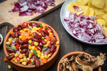 Mixture of vegetables, dried boletus mushrooms, sliced potato, red onion sliced and whole on a cutting board and spices, on old rustic wooden table.