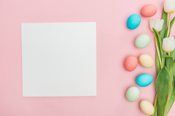 top view of tulips and pastel easter eggs isolated on pink with empty board