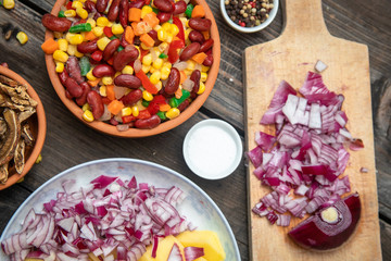 Mixture of vegetables, dried boletus mushrooms, sliced potato, red onion sliced and whole on a cutting board and spices, on old rustic wooden table.