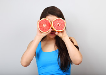 Beautiful makeup brunette woman covering fresh red grapefruit the eyes on blue background.