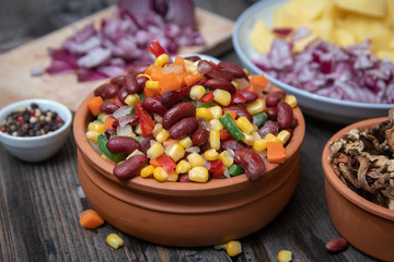 Mixture of vegetables, dried boletus mushrooms, sliced potato, red onion sliced and whole on a cutting board and spices, on old rustic wooden table.