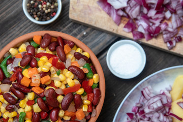 Mixture of vegetables, dried boletus mushrooms, sliced potato, red onion sliced and whole on a cutting board and spices, on old rustic wooden table.