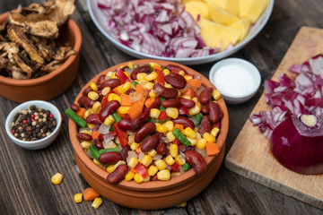 Mixture of vegetables, dried boletus mushrooms, sliced potato, red onion sliced and whole on a cutting board and spices, on old rustic wooden table.