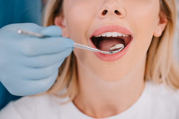 cropped view of dentist examining teeth of young woman with mouth mirror