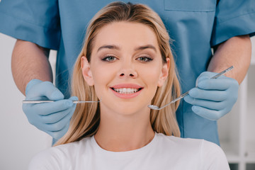 dentist holding mouth mirror and dental probe while young woman looking at camera