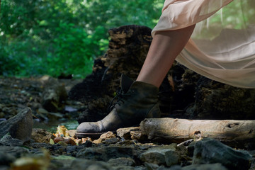 The legs of a young girl in a light summer dress and vintage shoes standing by a small stream on a clear sunny day in the forest. Through the thin dress the sun's rays shine