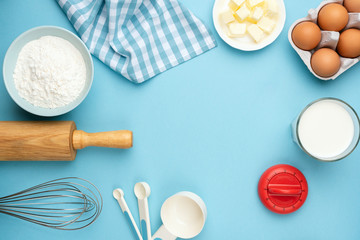 Baking ingredients on blue background. Rolling pin, flour, eggs, butter, measuring spoons and other...