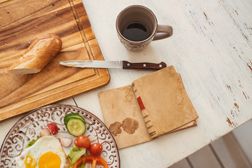 Reading a book at breakfast scrambled eggs, fresh vegetables knife and bread on a white rustic table